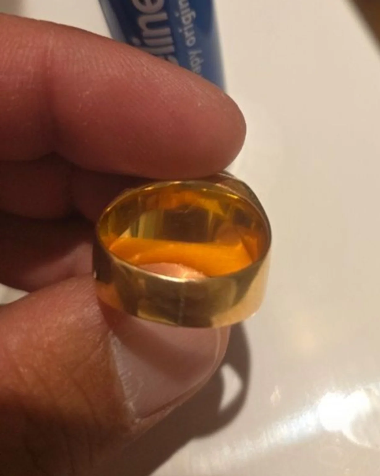 Bague dorée à anneau large tenue entre les doigts.