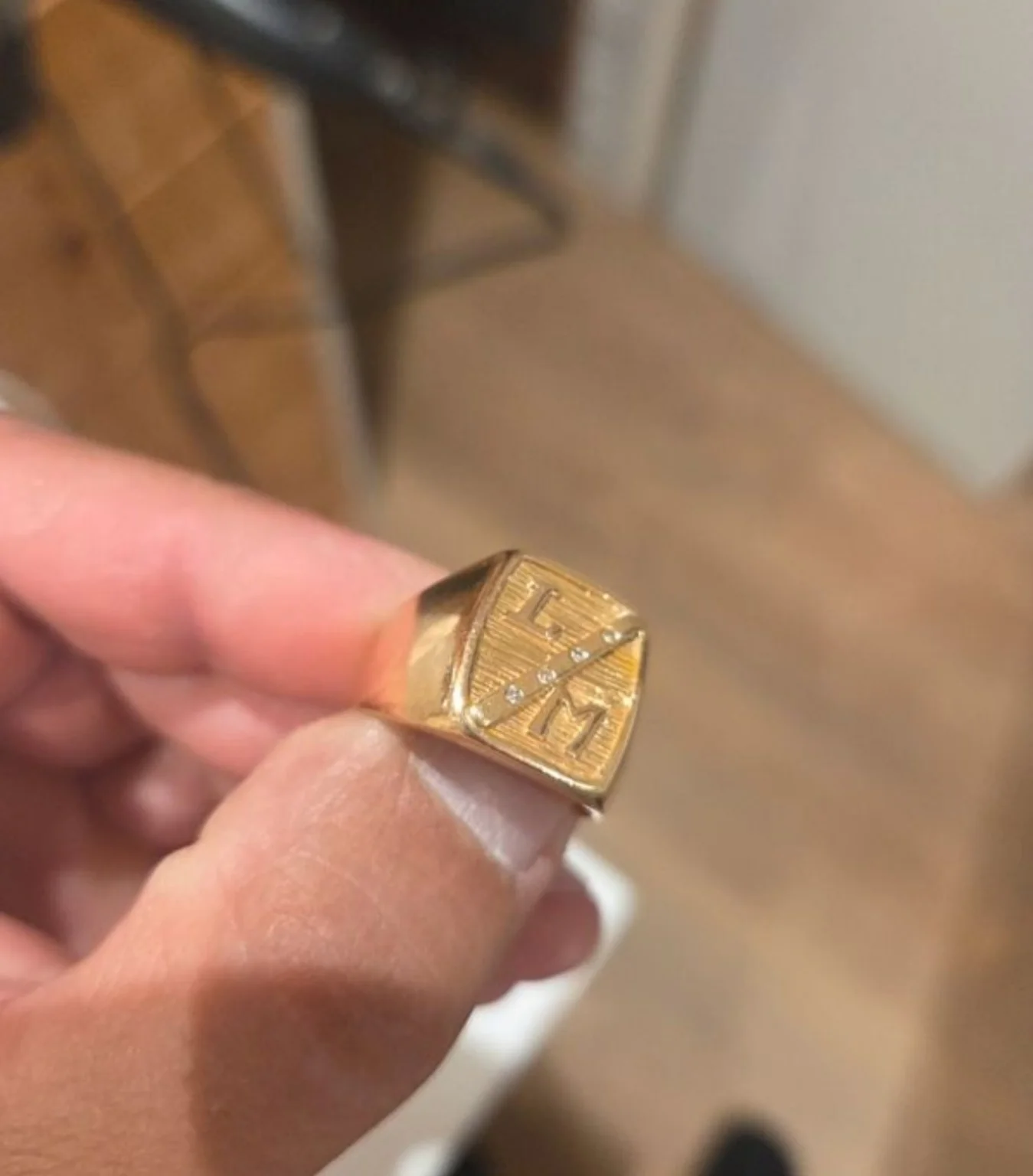 Chevalière dorée à face gravée, tenue entre les doigts.