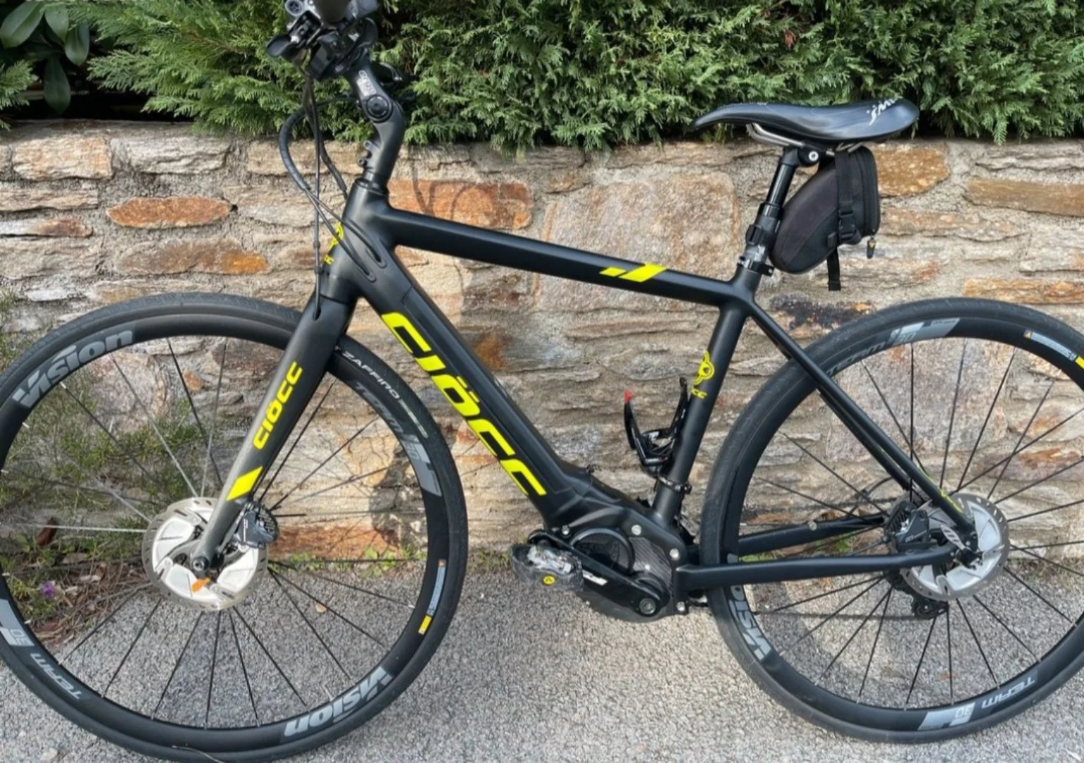Vélo électrique noir et jaune, photographié de profil près d’un muret.